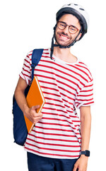 Young hispanic man wearing student backpack and bike helmet holding binder looking positive and happy standing and smiling with a confident smile showing teeth