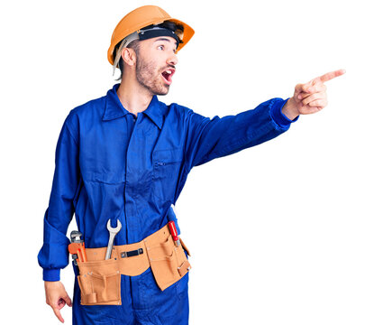 Young hispanic man wearing worker uniform pointing with finger surprised ahead, open mouth amazed expression, something on the front
