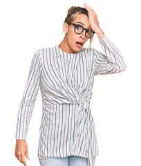 Beautiful blonde woman wearing business shirt and glasses surprised with hand on head for mistake, remember error. forgot, bad memory concept.