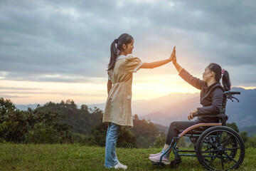 Happy young mother in wheelchair with care helper daughter arms up outstretched in spring nature at...