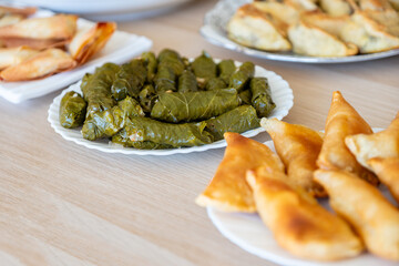 Dish of grape rolls on wooden table from top view with sambousek and qatayef