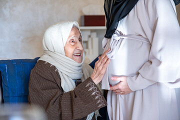 muslim old woman feeling excited for her new grandson touch her daughter tummy to feel fetus...