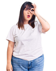 Young plus size woman wearing casual clothes doing ok gesture shocked with surprised face, eye looking through fingers. unbelieving expression.