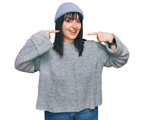 Young hispanic woman wearing cute wool cap smiling cheerful showing and pointing with fingers teeth and mouth. dental health concept.