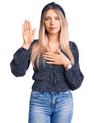 Young beautiful blonde woman wearing casual clothes swearing with hand on chest and open palm,...