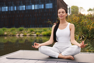 Naklejka na ściany i meble Beautiful young woman practicing Padmasana on yoga mat outdoors. Lotus pose