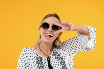 Portrait of hippie woman showing tongue and peace sign on yellow background