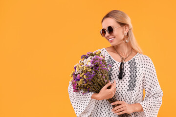Portrait of smiling hippie woman with bouquet of flowers on yellow background. Space for text