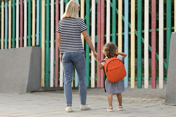 Woman and her little daughter on their way to kindergarten outdoors, back view - obrazy, fototapety, plakaty