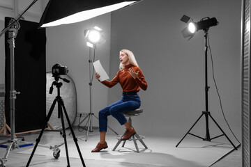Casting call. Emotional woman with script sitting on chair and performing in front of camera in studio - obrazy, fototapety, plakaty
