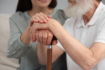 Senior man with walking cane and young woman indoors, closeup