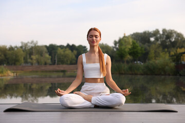 Fototapeta na wymiar Beautiful young woman practicing Padmasana on yoga mat outdoors. Lotus pose