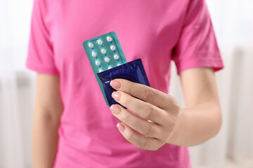 Woman holding condom and contraceptive pills on blurred background, closeup. Choosing birth control...