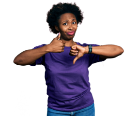 African american woman with afro hair wearing casual purple t shirt doing thumbs up and down, disagreement and agreement expression. crazy conflict