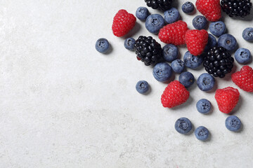 Many different fresh ripe berries on white textured table, flat lay. Space for text