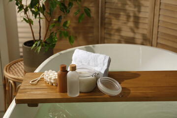 Wooden tray with spa products and towels on bath tub in bathroom. Space for text