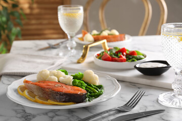 Healthy meal. Tasty grilled salmon with vegetables and lemon served on white marble table