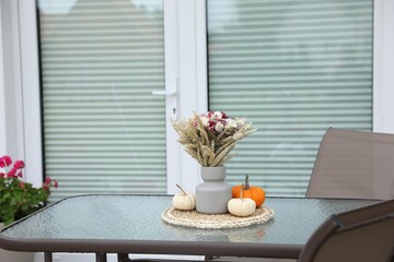 Beautiful bouquet of dry flowers and small pumpkins on glass table outdoors