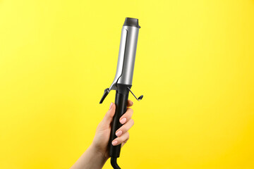 Hair styling appliance. Woman holding curling iron on yellow background, closeup