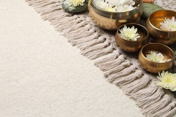 Tibetan singing bowls with water and beautiful chrysanthemum flowers on beige table, space for text