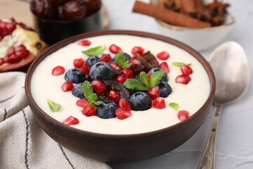 Delicious semolina pudding with blueberries, pomegranate, dates and mint in bowl on white table, closeup