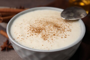 Delicious semolina pudding with cinnamon in bowl and spoon on table, closeup