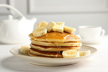 Delicious pancakes with bananas, honey and butter on white wooden table, closeup