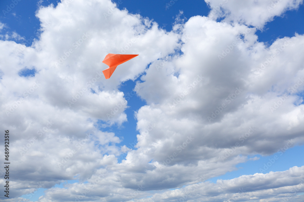 Wall mural Orange paper plane flying in blue sky with clouds