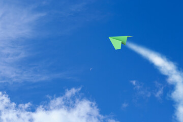 Green paper plane flying in blue sky with clouds