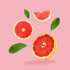 Pieces of grapefruit and green leaves falling on pink background