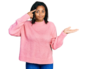 Beautiful hispanic woman wearing casual winter sweater confused and annoyed with open palm showing copy space and pointing finger to forehead. think about it.