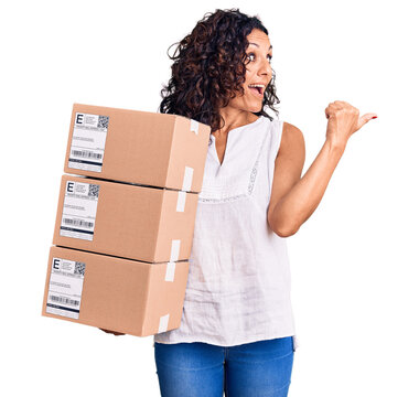Middle age beautiful woman holding delivery package pointing thumb up to the side smiling happy with open mouth