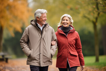 Elderly gray haired retired couple smile while walking outdoors in a park in autumn