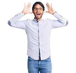 Handsome hispanic man wearing business shirt and glasses smiling cheerful playing peek a boo with hands showing face. surprised and exited