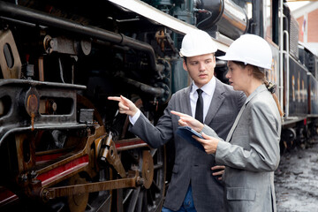 Young caucasian engineer man and woman in suit checking train with tablet in station, team engineer...