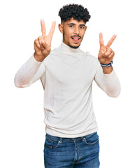 Young arab man wearing casual winter sweater smiling with tongue out showing fingers of both hands doing victory sign. number two.