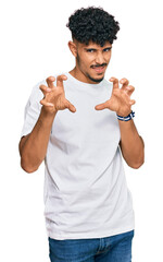Young arab man wearing casual white t shirt smiling funny doing claw gesture as cat, aggressive and...
