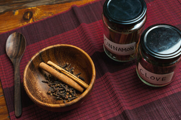a wooden bowl of cinnamon and clove with a spice glass jar with a name tag on the side concept of using spice in a kitchen