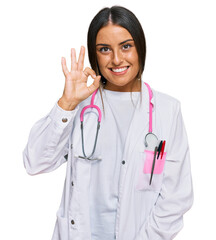 Beautiful hispanic woman wearing doctor uniform and stethoscope smiling positive doing ok sign with hand and fingers. successful expression.