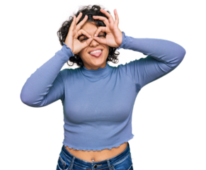 Young hispanic woman with curly hair wearing casual clothes doing ok gesture like binoculars sticking tongue out, eyes looking through fingers. crazy expression.