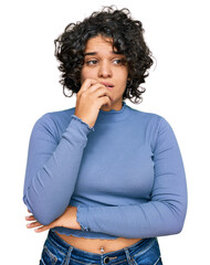 Fototapeta na wymiar Young hispanic woman with curly hair wearing casual clothes looking stressed and nervous with hands on mouth biting nails. anxiety problem.