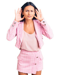Young beautiful latin girl wearing business clothes trying to hear both hands on ear gesture, curious for gossip. hearing problem, deaf