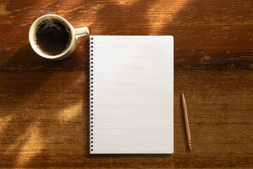 テーブルの上にある空白のノートブックと鉛筆、コーヒー。上からのアングル