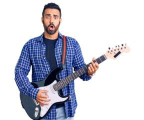 Young hispanic man playing electric guitar scared and amazed with open mouth for surprise, disbelief face