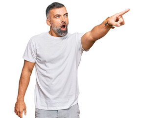 Middle age handsome man wearing casual white tshirt pointing with finger surprised ahead, open mouth amazed expression, something on the front