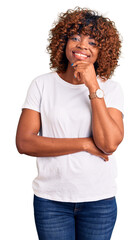 Fototapeta na wymiar Young african american woman wearing casual white tshirt looking confident at the camera with smile with crossed arms and hand raised on chin. thinking positive.