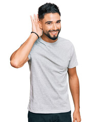Fototapeta premium Young man with beard wearing casual grey tshirt smiling with hand over ear listening an hearing to rumor or gossip. deafness concept.
