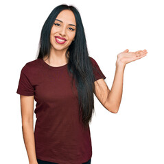 Fototapeta premium Young hispanic girl wearing casual t shirt smiling cheerful presenting and pointing with palm of hand looking at the camera.