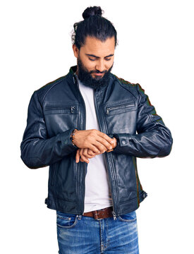 Young arab man wearing casual leather jacket checking the time on wrist watch, relaxed and confident