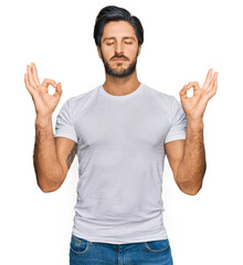 Young hispanic man wearing casual white t shirt relax and smiling with eyes closed doing meditation gesture with fingers. yoga concept.